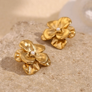 Detail view of 18K gold petal earrings with a white pearl on textured stone background