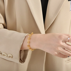Close-up of a chunky gold knot-link chain bracelet on a model wearing a neutral blazer