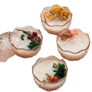 Set mit vier bernsteinfarbenen Duftkerzen mit Trockenblumen und Orangenscheiben auf Weiß