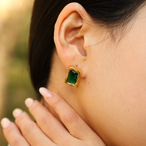 Close-up of a gold irregular rectangular earring with an emerald gemstone on a model