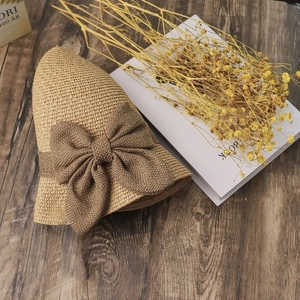 Straw sun hat with brown bow on wood background with dried flowers and books