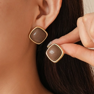 Vintage geometric leather stud earrings with gold trim and brown texture on model
