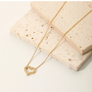 Detailed view of 18K gold plated heart pendant with zircon on beige stone display