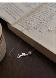 Dettaglio del bracciale gatto in argento S925 con perla su un libro d'epoca aperto
