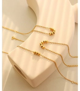 Close-up of 18K gold plated beaded anklet displayed on a minimalist beige sculpture stand