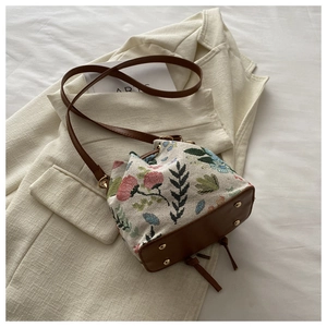 Detail of ethnic embroidered bucket bag with floral patterns on beige canvas and brown PU leather