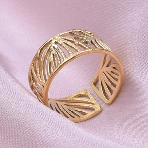 Vue macro d'une bague ajourée dorée sur fond de soie rose délicate