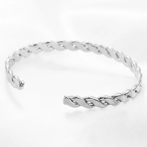 Macro shot of silver C-shaped twisted metal cuff bracelet on white silk fabric background