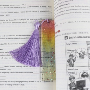 Close-up of resin bookmark with glitter gradient and purple tassel on open book
