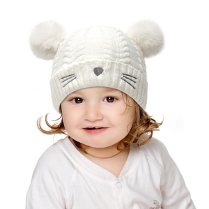 Detail of baby white knit hat with plush pompoms and cute cat whiskers embroidery