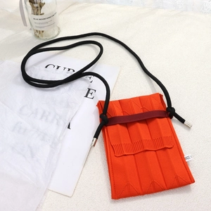 Detailed knit texture of orange accordion phone bag with black rope strap and tag