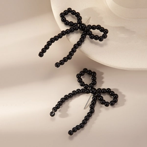 Detail of elegant black beaded bow earrings featuring glossy pearls on a beige surface