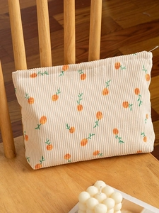Floral corduroy makeup bag in cream with orange flowers on a wooden chair