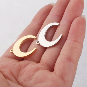 Polished moon crescent charms in gold and silver stainless steel held by hand