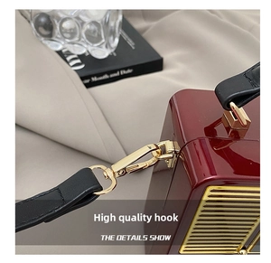 Detail of high-gloss burgundy radio bag featuring gold-tone metal hooks and stitching