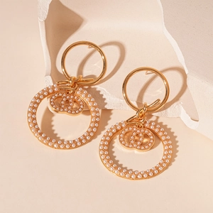 Detail showing gold knot earrings with micro pearls and double C geometric pendant