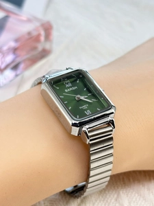 Detail of square green dial watch with silver bamboo-style elastic band on wrist