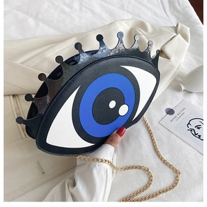 Detail of hip hop round bag with eye design and gold chain on white fabric
