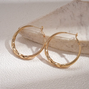 Detailed view of large gold hoop earrings with a textured wavy design on a white surface