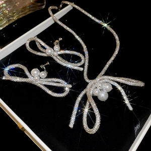 Detailed view of silver bowknot necklace and earrings set with sparkling pearls