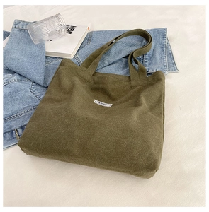 Detail of army green canvas tote bag on denim jacket with fashion label and book