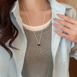 Detail of silver wire flower pendant with black bead on white cord necklace worn by model