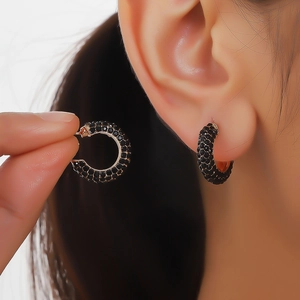 Macro shot of gold-plated C-shaped earrings encrusted with sparkling black cubic zirconia