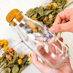 Detail showing a purple butterfly sticker being applied to a transparent glass bottle