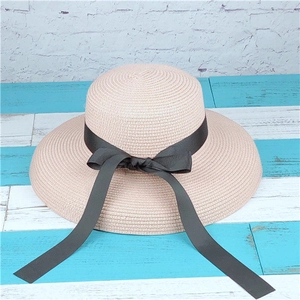 Close-up of beige straw sun hat featuring a wide flat brim and elegant black ribbon bow