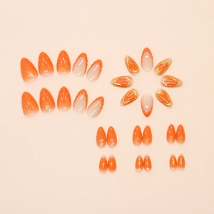 Detail of light orange almond press-on nails with French tips and pearl embellishments
