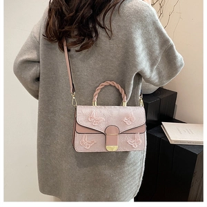 Détail d'un sac bandoulière rose brodé avec poignée tressée et motifs papillons