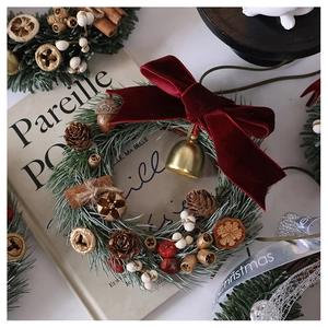 Detail of Christmas wreath with red velvet bow, pine cones, and golden bell ornaments