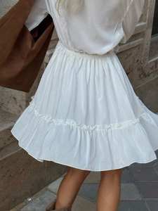 Detail of white V-neck dress featuring elastic smocked waist and ruffled hemline