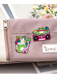 Close-up of cute pink frog enamel pins with headphones and radio on a purple canvas bag