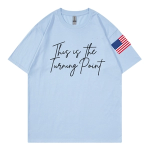 Dettaglio di una t-shirt in cotone azzurro con stampa corsiva e patch bandiera americana
