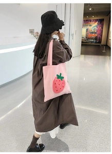 Detail of pink canvas tote bag featuring a 3D strawberry applique carried by a model