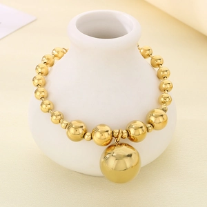Detail of a gold beaded bracelet with large sphere pendant on a white ceramic vase