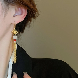 Detail of gold cloud-patterned tassel earrings with red beads on a model side profile