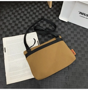 Detail view of khaki nylon messenger bag with orange label on grey checkered background
