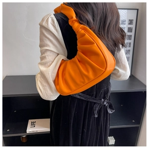 Detail of an orange pleated underarm bag showing the soft PU leather texture and fit
