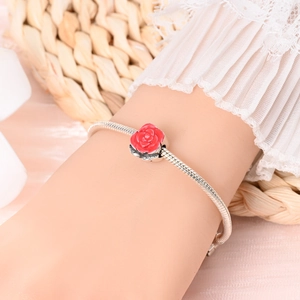 Close-up of a silver snake chain bracelet featuring a red enamel rose charm on a model's wrist