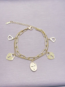 Detail eines goldenen Lagenarmbands mit Herzanhängern und einem Kreuzanhänger