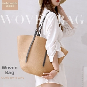 Detail view of khaki woven straw tote bag with slim dark leather shoulder straps on model