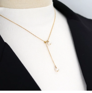 Detail view of Y-shaped gold necklace with natural pearls on a model in a black blazer