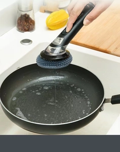 Détail d'une brosse à vaisselle avec réservoir de savon utilisée sur une poêle de cuisine