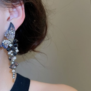 Detail view of long butterfly tassel earrings with blue zircon crystals on a model's ear