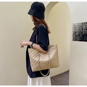 Detail of beige quilted tote bag with metallic chain strap and spacious interior design