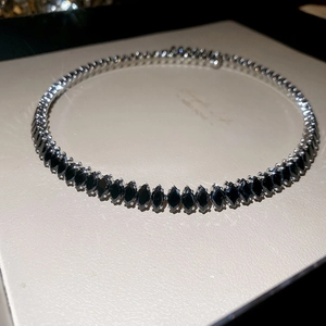 Macro shot of silver choker with marquise-cut black zircons on white leather texture