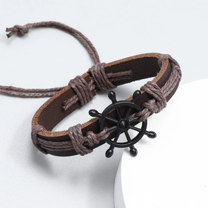 Detail view of woven brown leather bracelet featuring a black nautical helm centerpiece