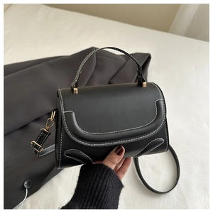 Detail of black small square handbag with white contrast stitching and gold metal buckle
